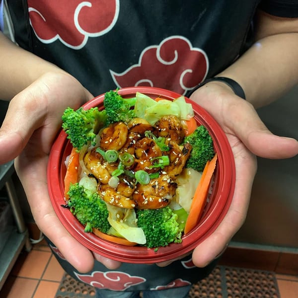 Hands holding a red bowl of Teriyaki J's shrimp, broccoli, and vegetables.