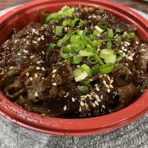 Teriyaki J's beef teriyaki bowl, topped with sesame seeds and chopped green onions in a red bowl.
