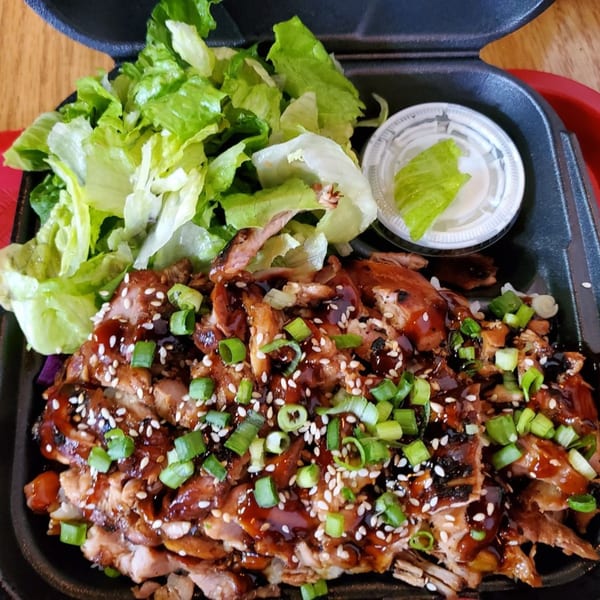 Teriyaki J's chicken teriyaki with rice, fresh lettuce, and a side of dressing in a takeout container.