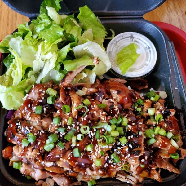 Teriyaki J's chicken teriyaki with green onions, sesame seeds, and a side salad in a takeout container.