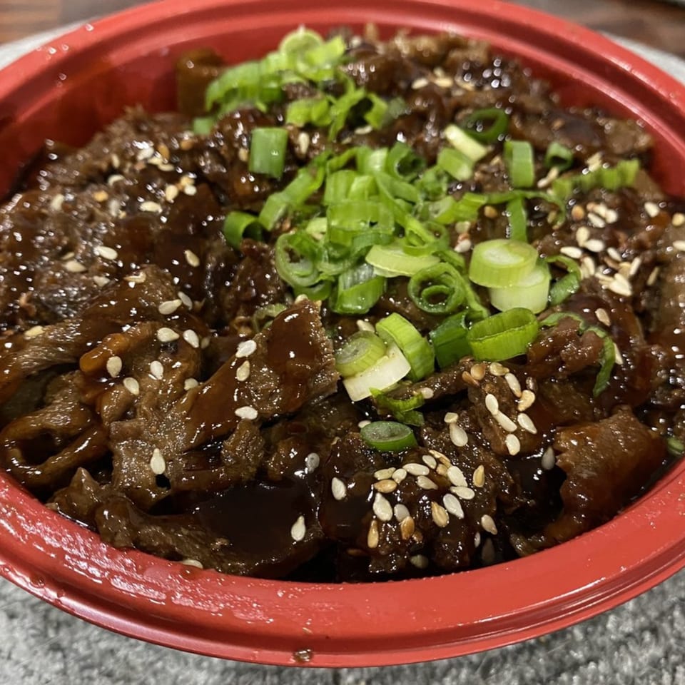 Teriyaki J's beef teriyaki bowl, garnished with sesame seeds and chopped green onions.