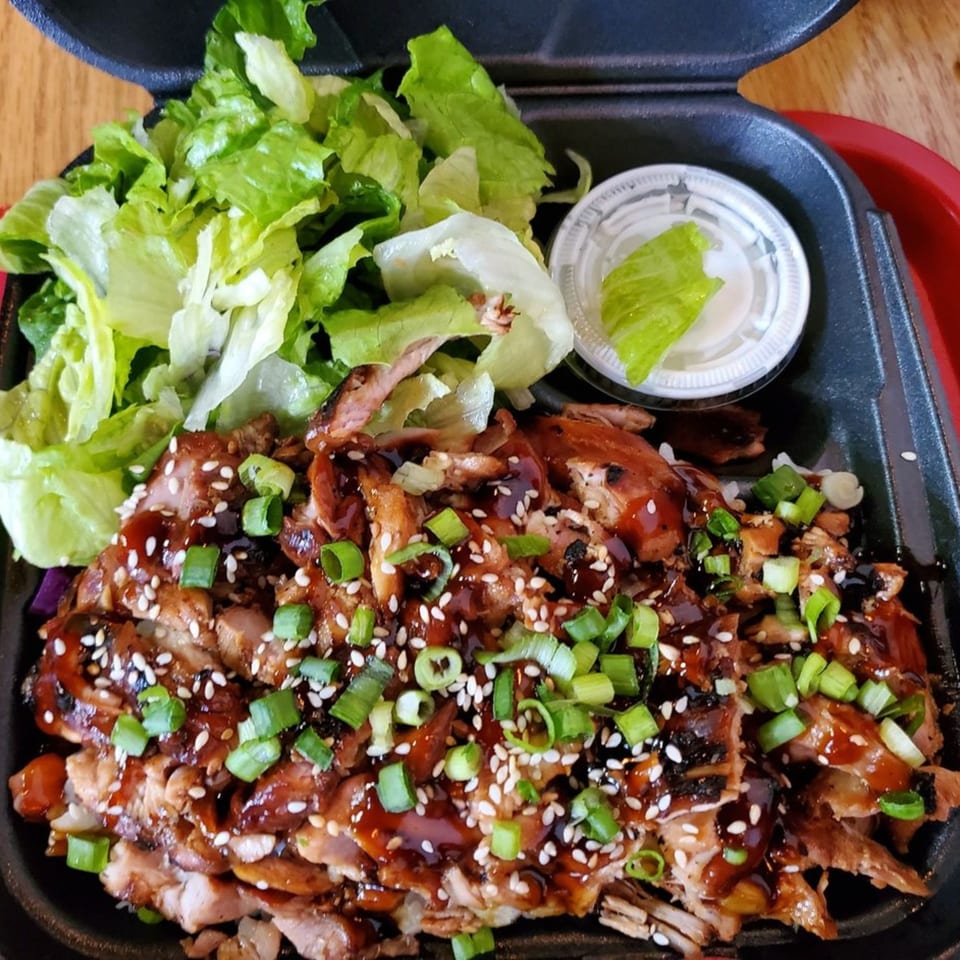 Teriyaki J's chicken teriyaki with green onions, sesame seeds, and a side salad in a to-go container.