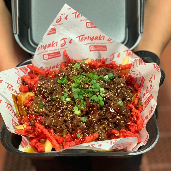 Teriyaki J's teriyaki beef, sesame seeds, and green onions over fries and red crunchy snacks.