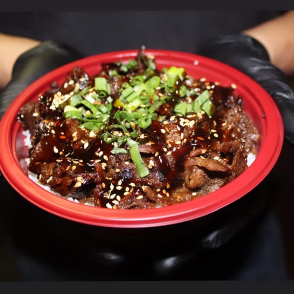 Teriyaki J's beef teriyaki bowl with green onions and sesame seeds, held by gloved hands.