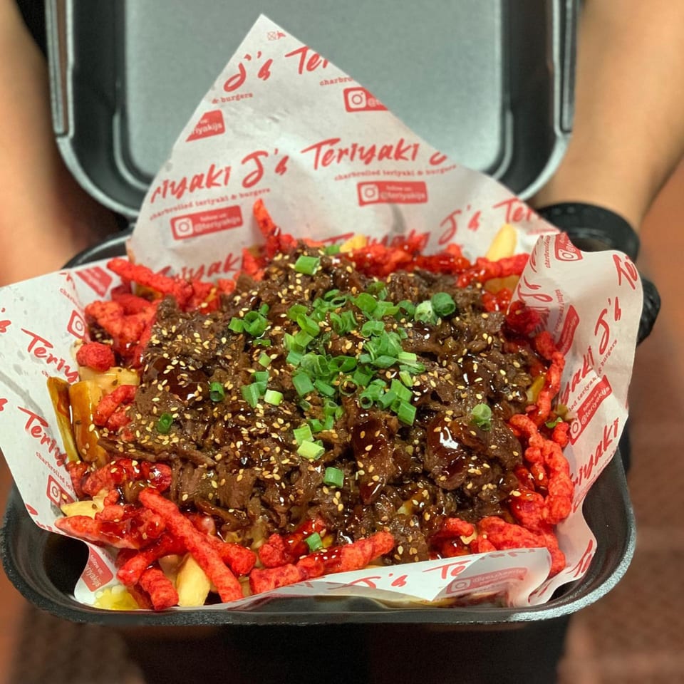 Teriyaki J's teriyaki beef, sesame seeds, and green onions over fries and red crunchy snacks.